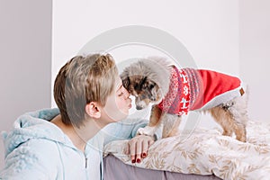 Young woman with short hair kissing cute puppy dog at home. Pet owner with little furry friend. Small pet dog licking its owner