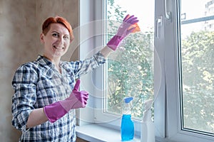 Young woman with short hair stands by window with hand thumb up. Cleaning service worker washes windows