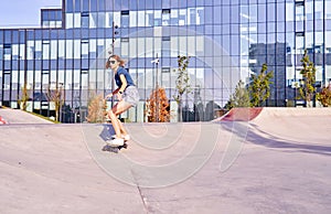 Young woman in short skirt skating on longboard outdoor in a skate park