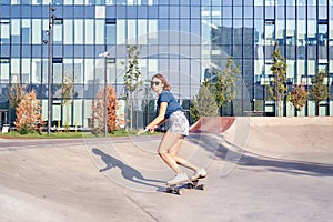 Young woman in short skirt skating on longboard outdoor in a skate park, doing the trick.