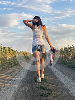 Young woman in shorts and white T-shirt is walking along country road