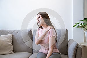 Young woman with shoulder pain. Young woman suffering shoulder neck ache tired sit on sofa at home