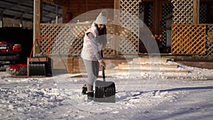 Young woman shoveling snow on backyard near the house .