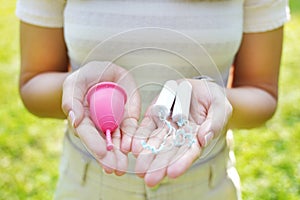 Young woman showing collector menstrual cup and tampons on her palm hands