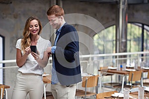 Young woman showing content on her cell phone to a man in restaurant, smiling. casual business outfit