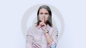 Young woman showing finger on lips gesture on white background