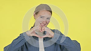 Young Woman showing Heart Shape by Hands on Yellow Background