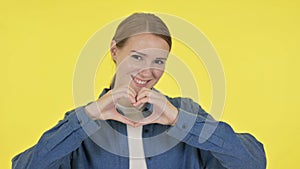 Young Woman showing Heart Shape by Hands on Yellow Background