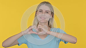 Young Woman showing Heart Shape by Hands on Yellow Background