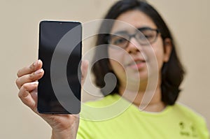 Young woman showing her blank mobile phone black screen against yellow background which can be used for copy space for different