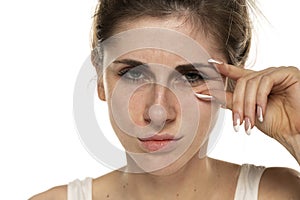 Young woman showing her eye wrinkles with her fingers on a white background