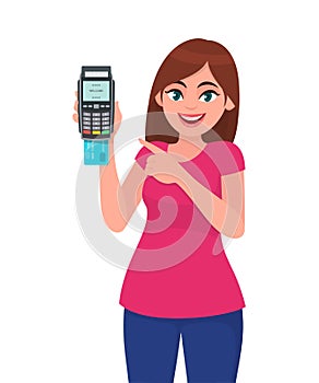 Young woman showing/holding pos payment terminal or credit/debit cards swiping machine and pointing finger. Wireless modern bank.