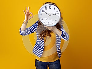 Young woman showing ok gesture holding clock in front of face