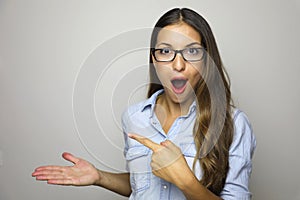 Young woman showing product with open hand palm and pointing finger. Excited expression on businesswoman wearing glasses isolated