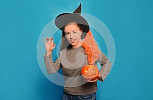 Young woman showing scary boo gesture or boo sign, holding Halloween pumpkin and looking at camera on a blue background.