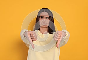 Young woman showing thumbs down on orange background