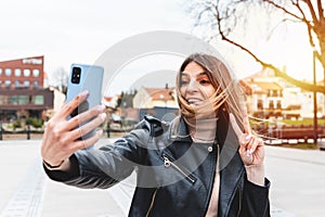 Young woman showing victory sign during video call on smart phone at city park.woman holding smartphone and showing V victory sign