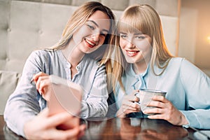 Young woman shows photos to her girlfriend in cafe