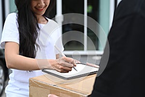 Young woman signing on digital tablet receipt of delivery package from delivery man.