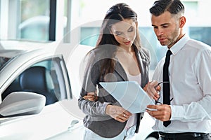 Young Woman Signing Documents at Car Dealership with Salesman