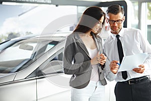 Young Woman Signing Documents at Car Dealership with Salesman