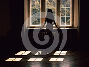Young woman silhouette, looking through the window