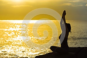 Young woman silhouette meditating and practicing yoga on the beach at sunset.Slim girl with yoga.