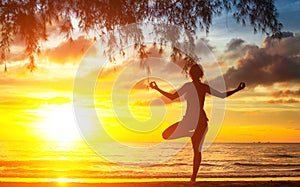 Young woman silhouette practicing yoga on beach.