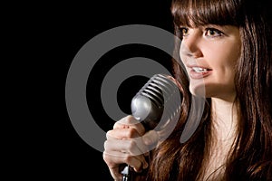 Young woman sing in microphone isolated on black