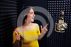 Young woman sings in the headphones on black background. Professional microphone golden with white colors. Recording vocals in a