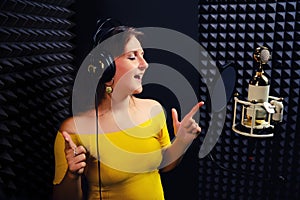 Young woman sings in the headphones on black background. Professional microphone golden with white colors. Recording vocals in a photo