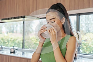 Young woman sips beverage in kitchen