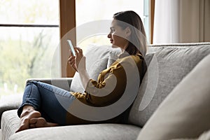 Young woman sit on couch spend leisure using smartphone