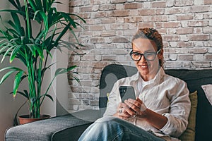 Young woman sit relax on sofa in living room browsing surfing wireless internet on smartphone, millennial girl rest on couch at