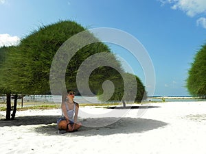 Young woman sit on the sand on a tropical sandy beach in the shade of trees. Malibu Beach, Koh Phangan, Thailand