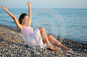 Young woman sits ashore of sea with rised hands photo