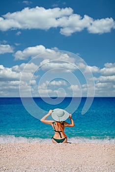 Young woman sits on beach and looks at sea, rear view