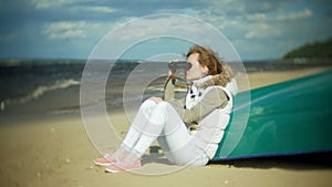 Young woman sits on the beach outside of the boat and looks through binoculars