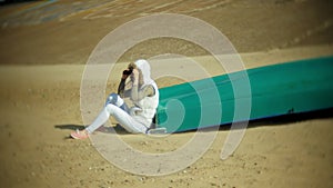 Young woman sits on the beach outside of the boat and looks through binoculars