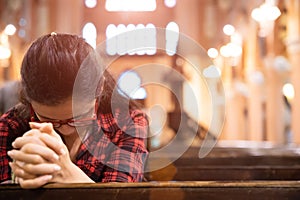 Young woman sits on a bench in the church and prays to God. Hands folded in prayer concept for faith photo