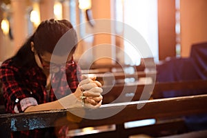 Young woman sits on a bench in the church and prays to God. Hands folded in prayer concept for faith