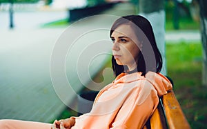 Young woman sits on bench in park. Adult female enjoys her rest on fresh air.