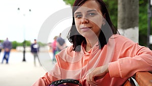 Young woman sits on bench in park. Adult female enjoys her rest on fresh air.