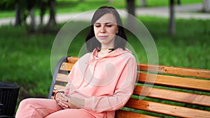 Young woman sits on bench in park. Adult female enjoys her rest on fresh air.