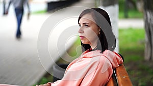 Young woman sits on bench in park. Adult female enjoys her rest on fresh air.