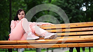 Young woman sits on bench in park. Adult female enjoys her rest on fresh air.