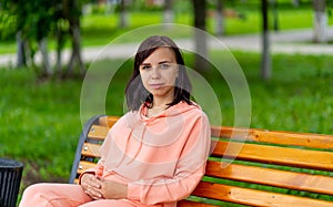 Young woman sits on bench in park. Adult female enjoys her rest on fresh air.