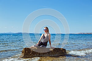 Young woman  sits on a boulder in the sea