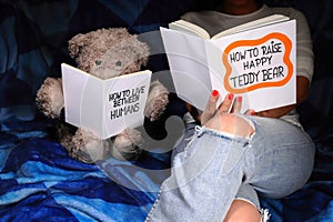 Young woman sits on the couch and reads a book. Next to her sits a Teddy Bear, cute evening reading book time concept.