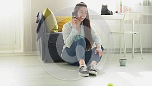 a young woman sits on the floor at home and talking on the phone